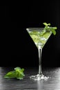 Delicious, refreshing green cocktail with ice, peppermint leaves and lime slices on a black stone surface