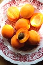 Delicious ripe apricots in a plate on the table on a sunny day, close-up, vertical. Pile of fresh whole juicy orange apricots and