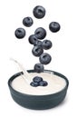 Delicious ripe blueberries falling into bowl with yogurt on white background