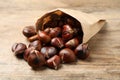 Delicious roasted edible chestnuts in paper bag on wooden table, closeup Royalty Free Stock Photo