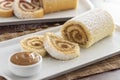 Delicious roll cake with caramel dulce de leche and sugar sliced on white platter and blurred background