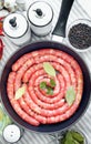 Delicious rustic raw meat sausages in frying pan, with bay leaves and fresh herbs in the kitchen. Royalty Free Stock Photo