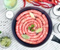 Delicious rustic raw meat sausages in frying pan, with bay leaves and fresh herbs in the kitchen. Royalty Free Stock Photo