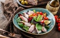 Delicious salad with sliced of turkey ham, grilled zucchini, tomatoes, basil, greens, olives and oil in bowl on wooden background Royalty Free Stock Photo