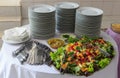 Delicious salad of vegetables and fruits. Lettuce, tomato, parsley, arugula, grape, mango, melon. On the table a pile of plates,