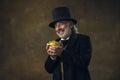 Handsome elderly gray-haired man, gentleman, aristocrat or actor eating fast food isolated on dark vintage background Royalty Free Stock Photo