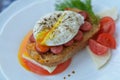 Delicious sandwich with open poached egg, meat, feta cheese, tomato, herbs, pepper - fast breakfast in cafe