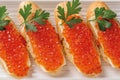 Delicious sandwiches with salmon caviar and parsley on a plate. Close-up of trout red caviar on a slice of french baguette with
