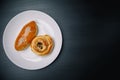 Delicious sesame buns or pies on white plate standing on black wooden table background. Tasty unhealthy snack for lunch or Royalty Free Stock Photo