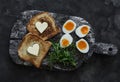 Delicious simple breakfast - boiled eggs with soft yolk, arugula, toast with butter on a rustic cutting board on a dark background Royalty Free Stock Photo