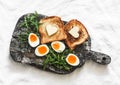 Delicious simple breakfast - boiled eggs with soft yolk, arugula, toast with butter on a rustic cutting board on a light