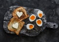 Delicious simple breakfast, snack - boiled eggs with soft yolk, toast with butter on a rustic cutting board on a dark background Royalty Free Stock Photo