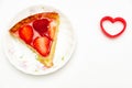 Delicious slice homemade strawberry tart with heart-shaped object on the side.