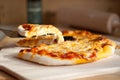 Home made cheese pizza with a slice being lifted from a wooden platter