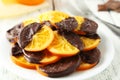 Delicious slices of orange coated chocolate on plate on a white wooden background