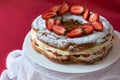 Delicious strawberries cream cake decorated with fresh cut strawberries on a white plate on the red background. Royalty Free Stock Photo