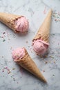 Delicious strawberry ice cream cone decorated with sugar rainbow sprinkles on marble background. top view Royalty Free Stock Photo