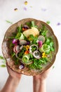 Delicious summer salad with edible flowers, vegetables, fruit, microgreens and cheese. Woman holding plate with salad, top view.