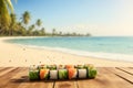 Delicious sushi cubes with avocado, salmon and cucumber on wooden plate on table on the beach, with the sea and palms in the Royalty Free Stock Photo