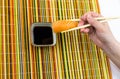 A delicious sushi rice and a slice of salmon, holding bamboo sticks in his hand, is lowered into a bowl with soy sauce on a multic