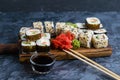 Delicious sushi rolls with fish, spinach, cheese, sesame seeds, eel, ginger, soy sauce and wasabi on a wooden board on a gray Royalty Free Stock Photo