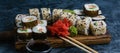 Delicious sushi rolls with fish, spinach, cheese, sesame seeds, eel, ginger, soy sauce and wasabi on a wooden board Royalty Free Stock Photo