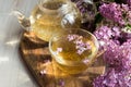 Delicious sweet herbal tea with lilac scent, glass cup and teapot with hot drink