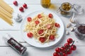 Delicious tagliatelle pasta with cherry tomatoes and basil on a white plate on a wooden table along with pasta ingredients: olives