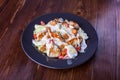 Delicious and tender salad with chicken and fresh vegetables dressed with sauce in a black plate on wooden table