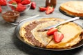 Delicious thin pancakes with chocolate paste and strawberries on grey table