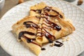 Delicious thin pancakes with chocolate spread, banana and nuts on plate, closeup