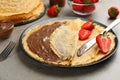 Delicious thin pancakes with chocolate spread and raspberries on grey table, closeup