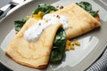 Delicious thin pancakes with spinach and sour cream on plate