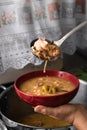 Delicious typical Central American dish called pozole being served by an adult lady with a metal ladle in a red bowl and a pot Royalty Free Stock Photo