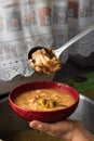 Delicious typical Central American dish called pozole served by an adult cook with a metal ladle in a red bowl and a pot almost Royalty Free Stock Photo