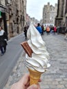 A delicious vanilla Soft serve in waffle cone in a hand Background of blur classic European street.