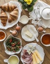 Delicious varied breakfast, brunch - croissants, eggs, ham, cheese, butter, apricot jam, fresh vegetable salad, tea on a wooden Royalty Free Stock Photo