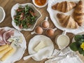 Delicious varied breakfast, brunch - croissants, eggs, ham, cheese, butter, apricot jam, fresh vegetable salad on a wooden table, Royalty Free Stock Photo