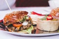 Delicious vegan black bean burger with vegetables and hummus, selective focus
