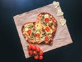 Delicious vegetarian heart shaped pizza with tomatoes, vegetables and cheese for Valentine`s Day on black background. Royalty Free Stock Photo