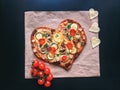 Delicious vegetarian heart shaped pizza with tomatoes, vegetables and cheese for Valentine`s Day on black background. Royalty Free Stock Photo