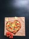 Delicious vegetarian heart shaped pizza with tomatoes, vegetables and cheese for Valentine`s Day on black background. Royalty Free Stock Photo