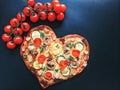 Delicious vegetarian heart shaped pizza with tomatoes, vegetables and cheese for Valentine`s Day on black background. Royalty Free Stock Photo