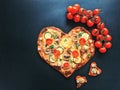 Delicious vegetarian heart shaped pizza with tomatoes, vegetables and cheese for Valentine`s Day on black background. Royalty Free Stock Photo