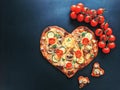 Delicious vegetarian heart shaped pizza with tomatoes, vegetables and cheese for Valentine`s Day on black background. Royalty Free Stock Photo