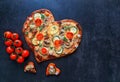 Delicious vegetarian heart shaped pizza with tomatoes, vegetables and cheese for Valentine`s Day on black background. Royalty Free Stock Photo