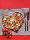 Delicious vegetarian heart shaped pizza with tomatoes, vegetables and cheese for Valentine`s Day on red background. Royalty Free Stock Photo
