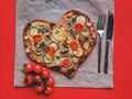 Delicious vegetarian heart shaped pizza with tomatoes, vegetables and cheese for Valentine`s Day on red background. Royalty Free Stock Photo