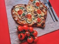 Delicious vegetarian heart shaped pizza with tomatoes, vegetables and cheese for Valentine`s Day on red background. Royalty Free Stock Photo