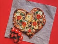 Delicious vegetarian heart shaped pizza with tomatoes, vegetables and cheese for Valentine`s Day on red background. Royalty Free Stock Photo